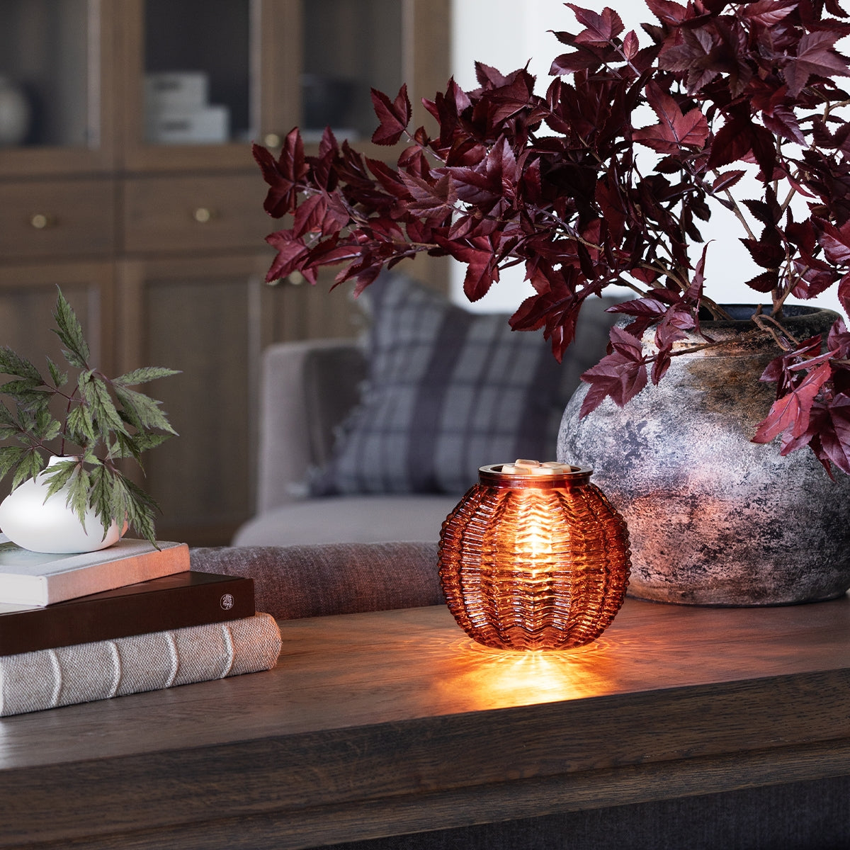 Decorative candle holder on a wooden surface with plants and books in the background