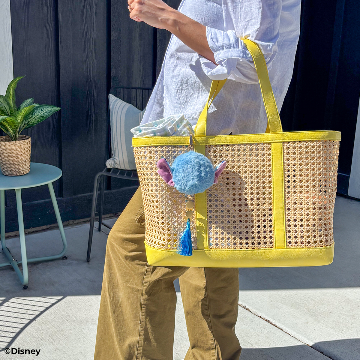 Person holding a yellow and wicker tote bag with a blue plush toy, outdoor setting.