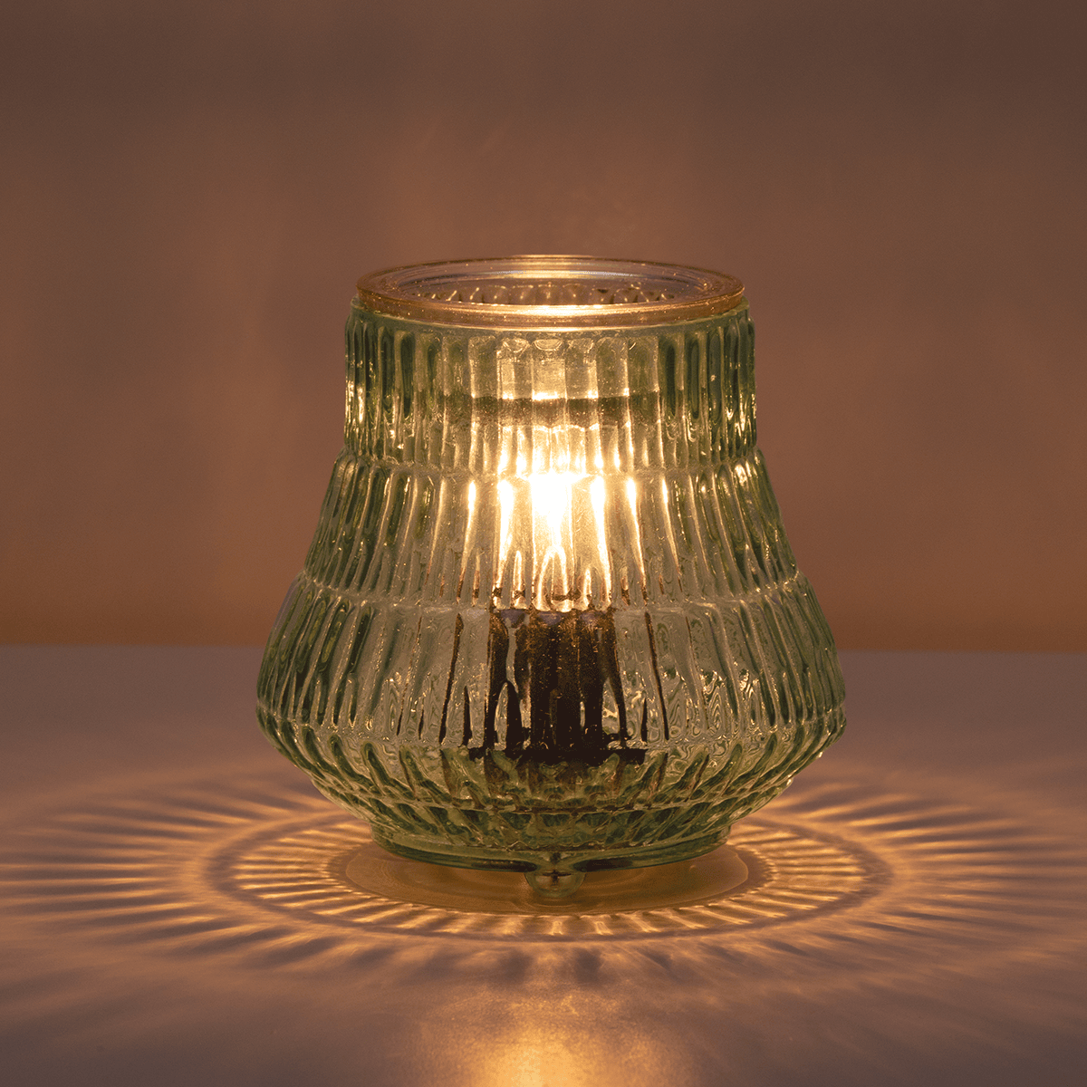 Green textured glass lantern with warm light on a neutral background