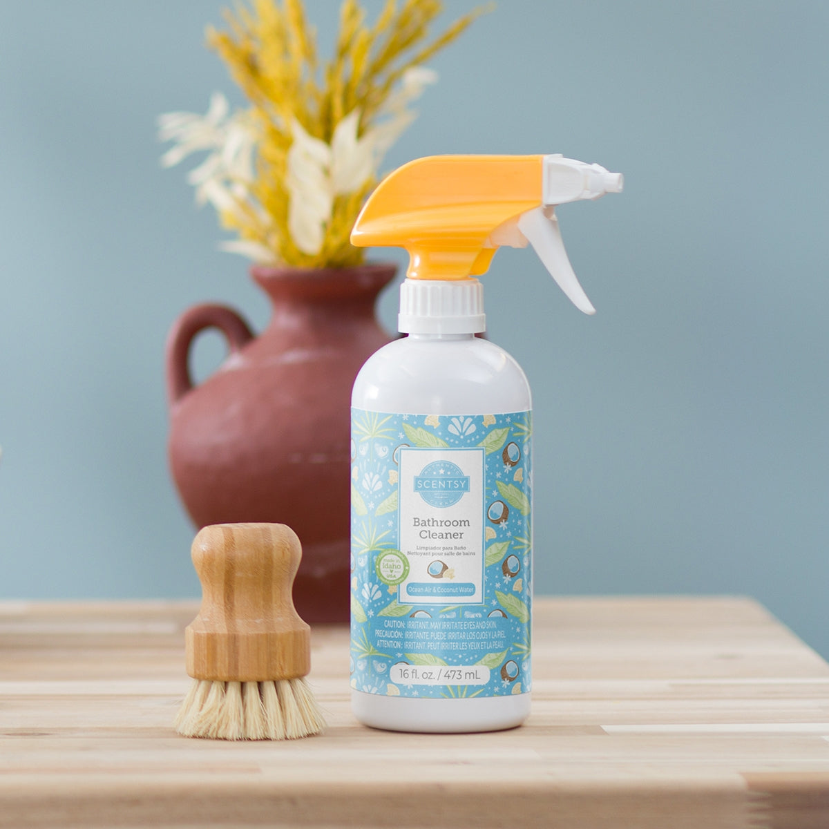 Bottle of bathroom cleaner with a brush and decorative vase on a wooden surface.