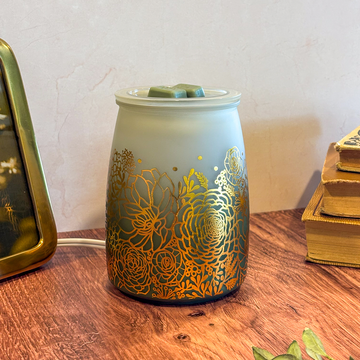 Decorative wax warmer with gold floral patterns on a wooden surface