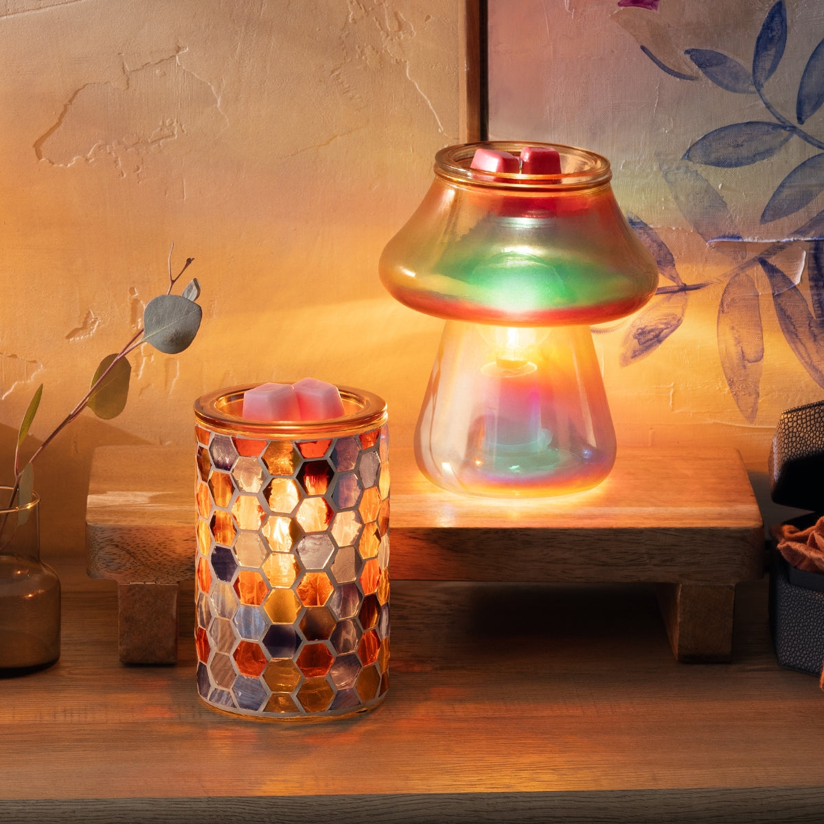 Two colorful glass candle holders on a wooden surface with a warm glow.