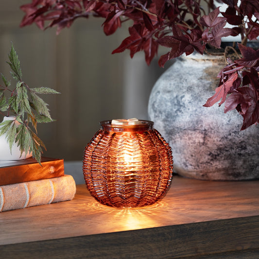 Decorative glass lantern with wicker texture on a wooden surface with plants in the background