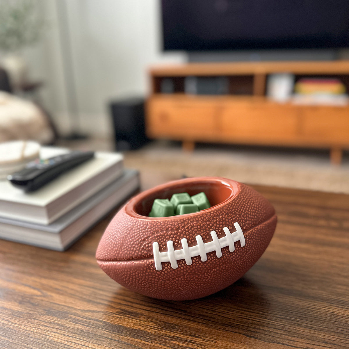 Football-shaped container with green cubes on a wooden table in a living room setting.