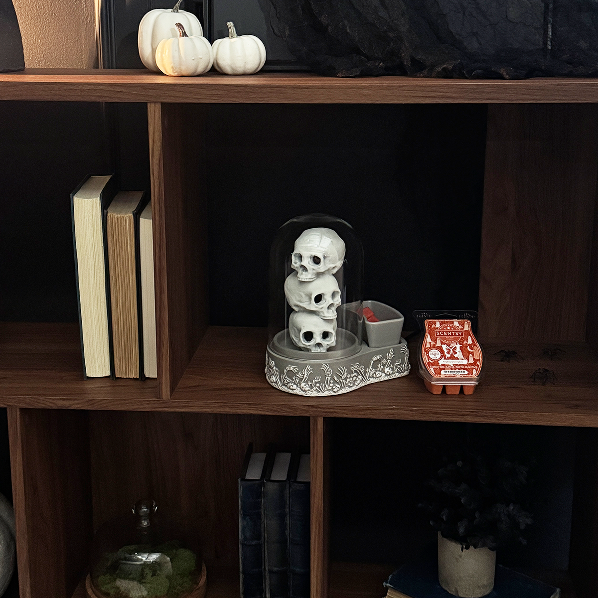 Decorative skull figurine on a wooden shelf with books and small pumpkins.
