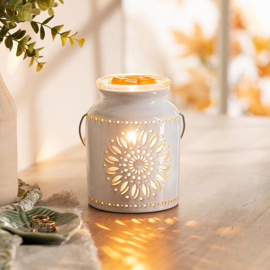 Decorative white lantern with floral cutout on a wooden surface, emitting warm light.