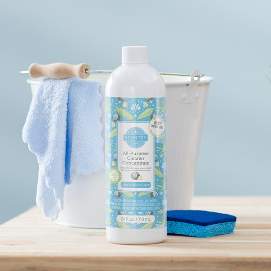 Scentsy all-purpose cleaner concentrate bottle with a blue towel and sponge on a wooden surface.