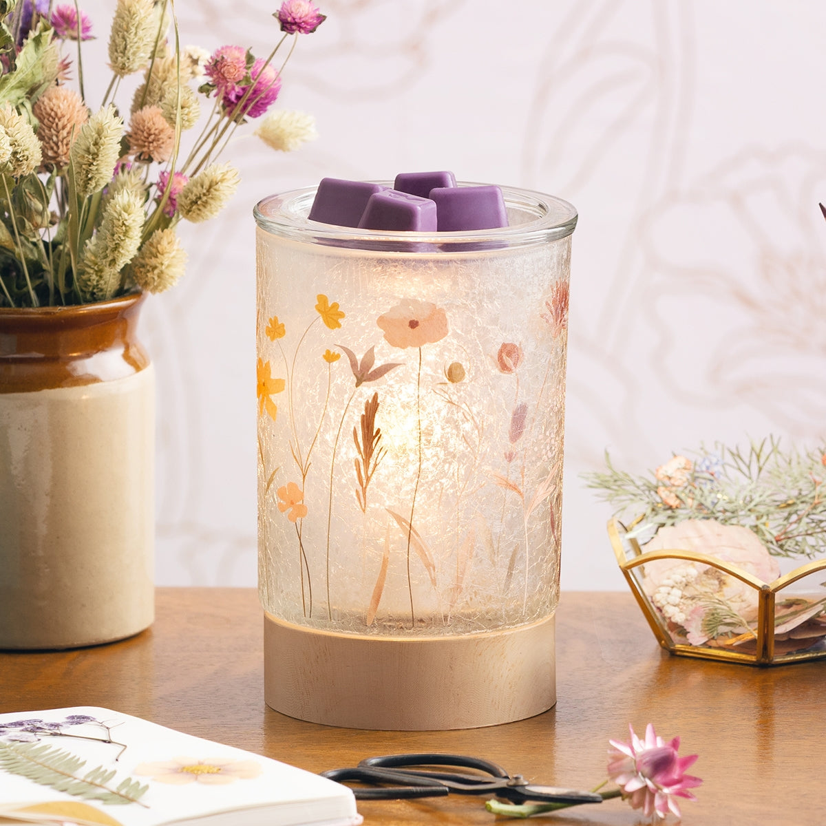 Decorative lamp with floral design on a wooden surface, surrounded by flowers and a book.