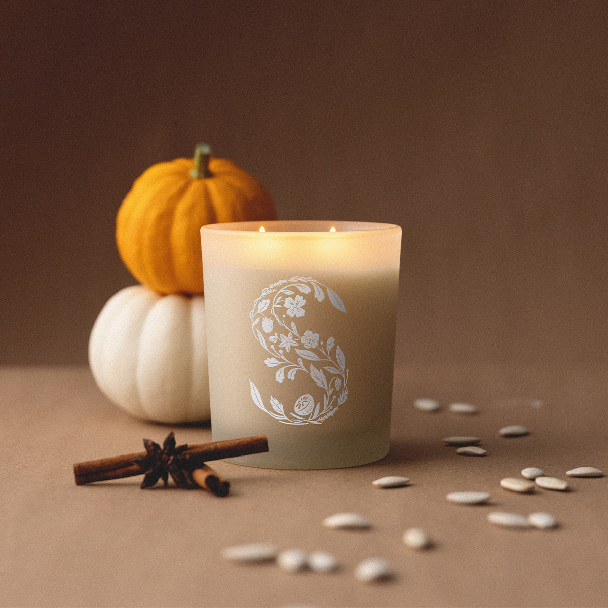 Candle with floral design, pumpkins, and cinnamon sticks on a brown background
