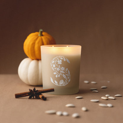 Candle with floral design, pumpkins, and cinnamon sticks on a brown background