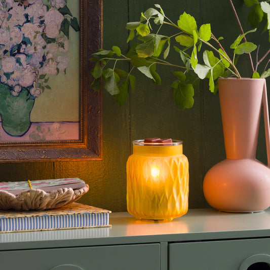 Decorative setup with a lit candle, vase, and framed artwork on a shelf.