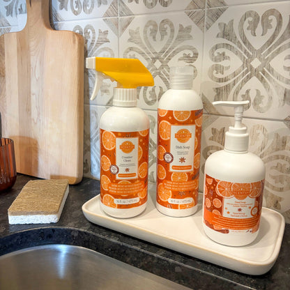 Three bottles of cleaning products with orange labels on a kitchen counter.