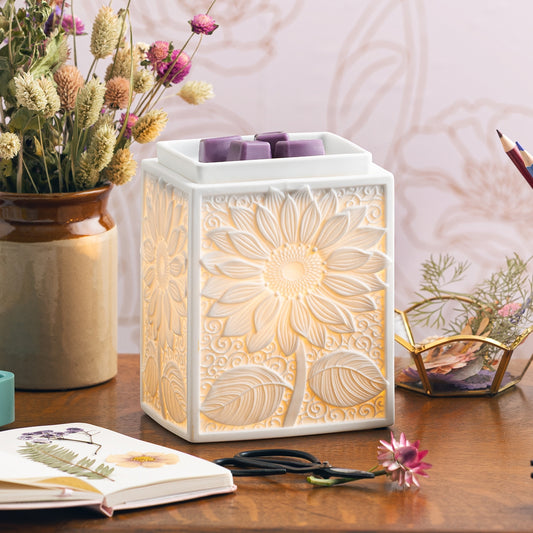 Decorative wax warmer with floral design on a table with flowers and stationery.
