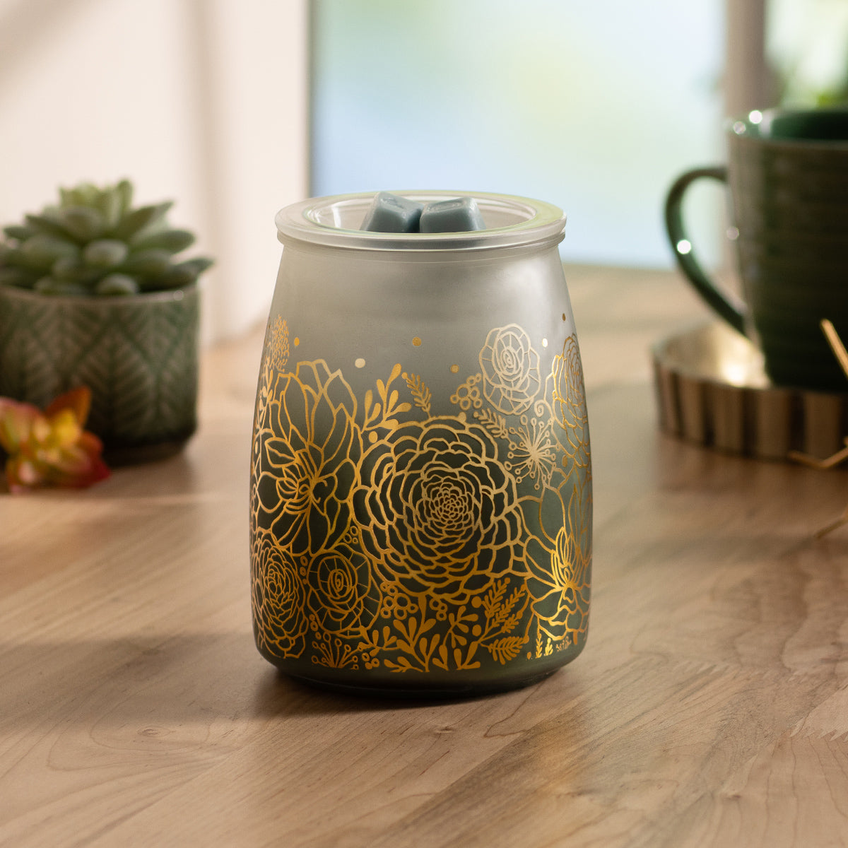 Decorative wax warmer with gold floral patterns on a wooden surface.