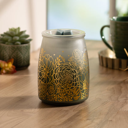 Decorative wax warmer with gold floral patterns on a wooden surface.